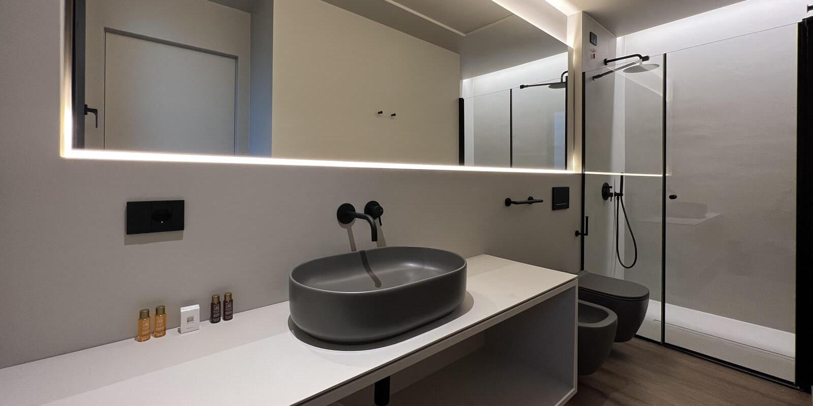 Modern bathroom with grey sink, glass shower, and backlit mirror.
