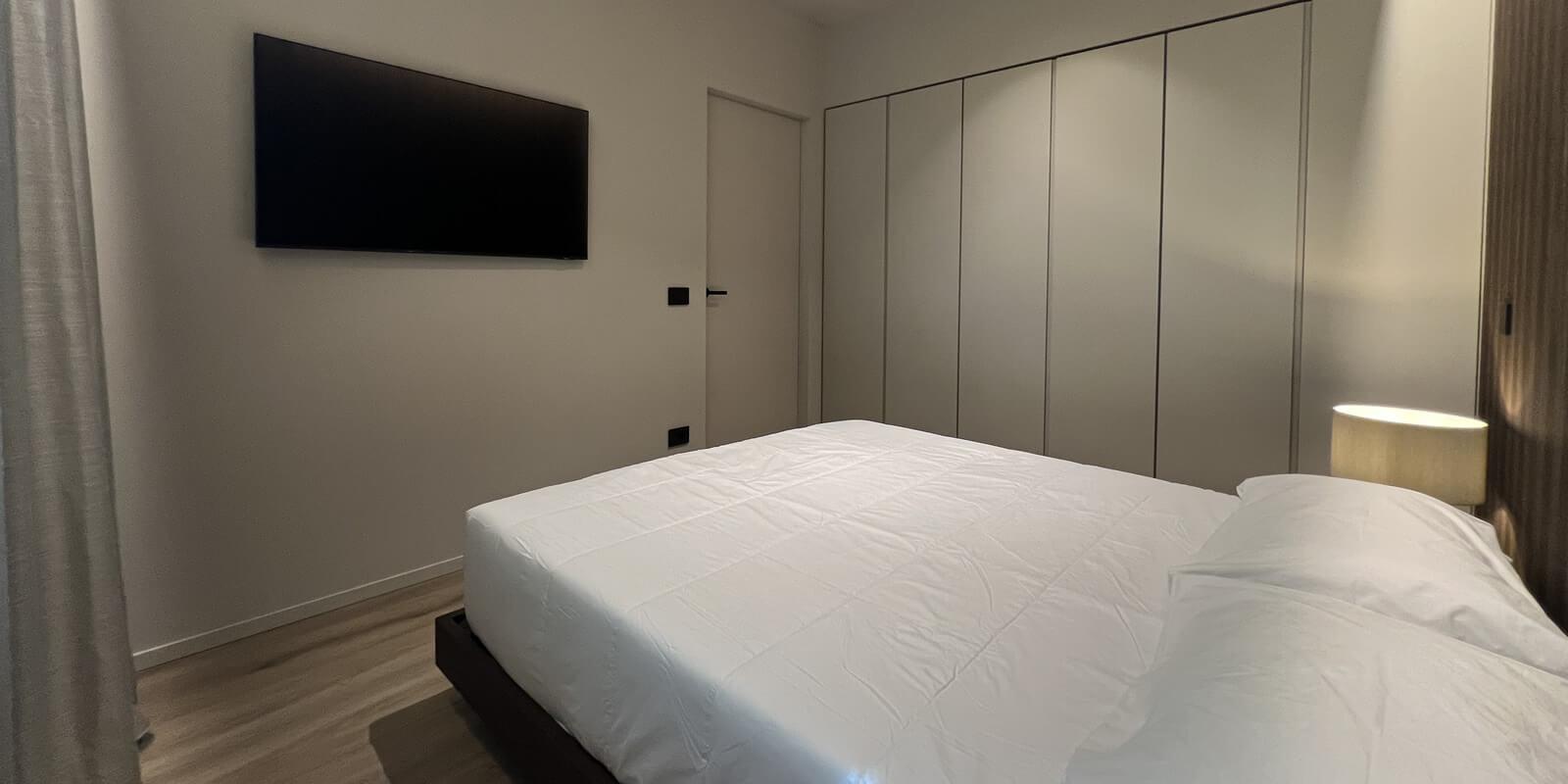 Modern room with a double bed, wall-mounted TV, and built-in wardrobe.