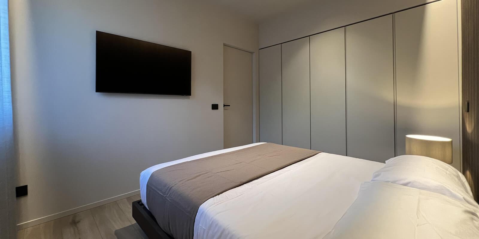 Modern bedroom with a double bed, wall-mounted TV, and built-in wardrobe.