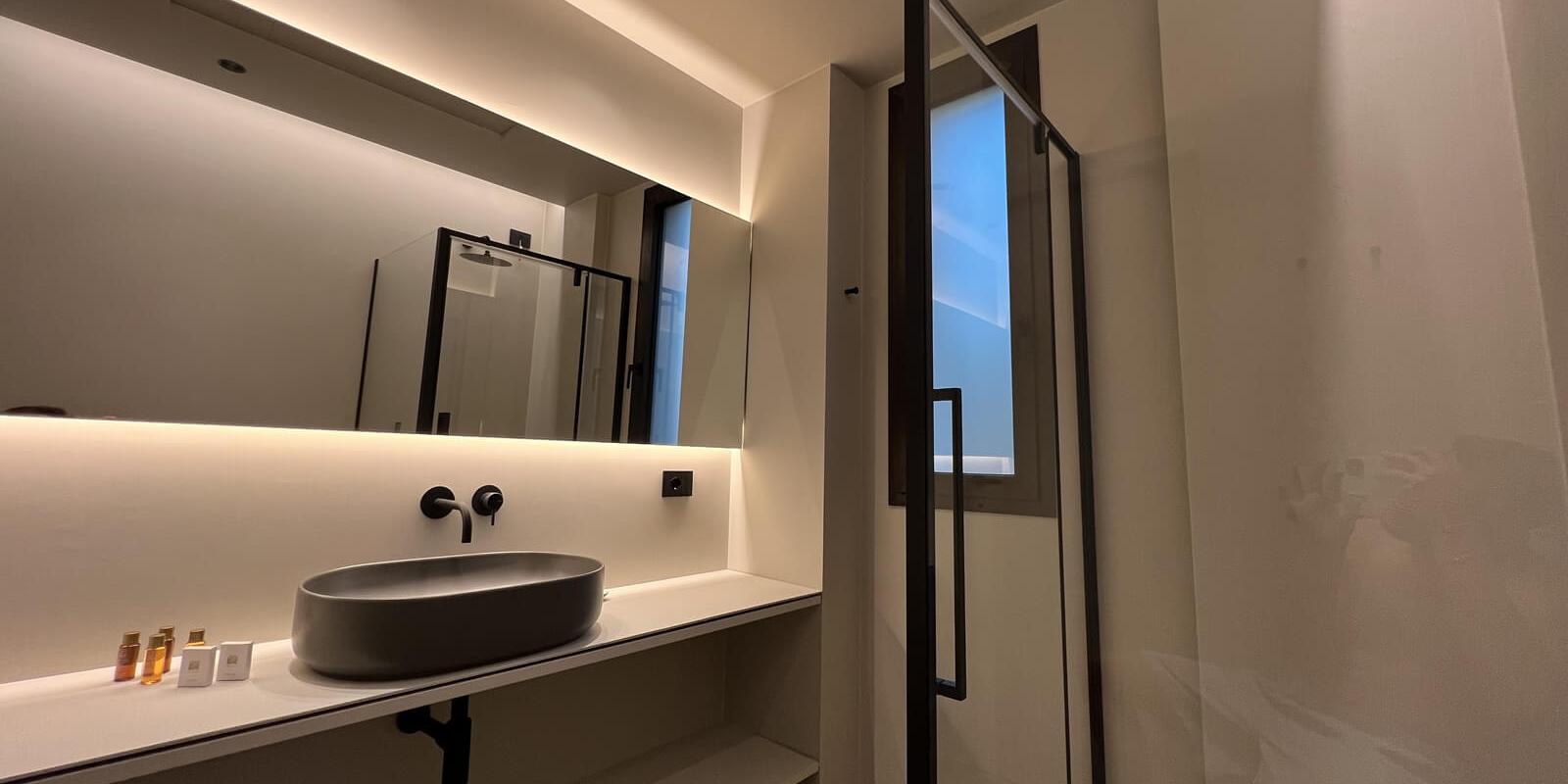 Bagno moderno con lavabo grigio, doccia a vetro e illuminazione soffusa.
